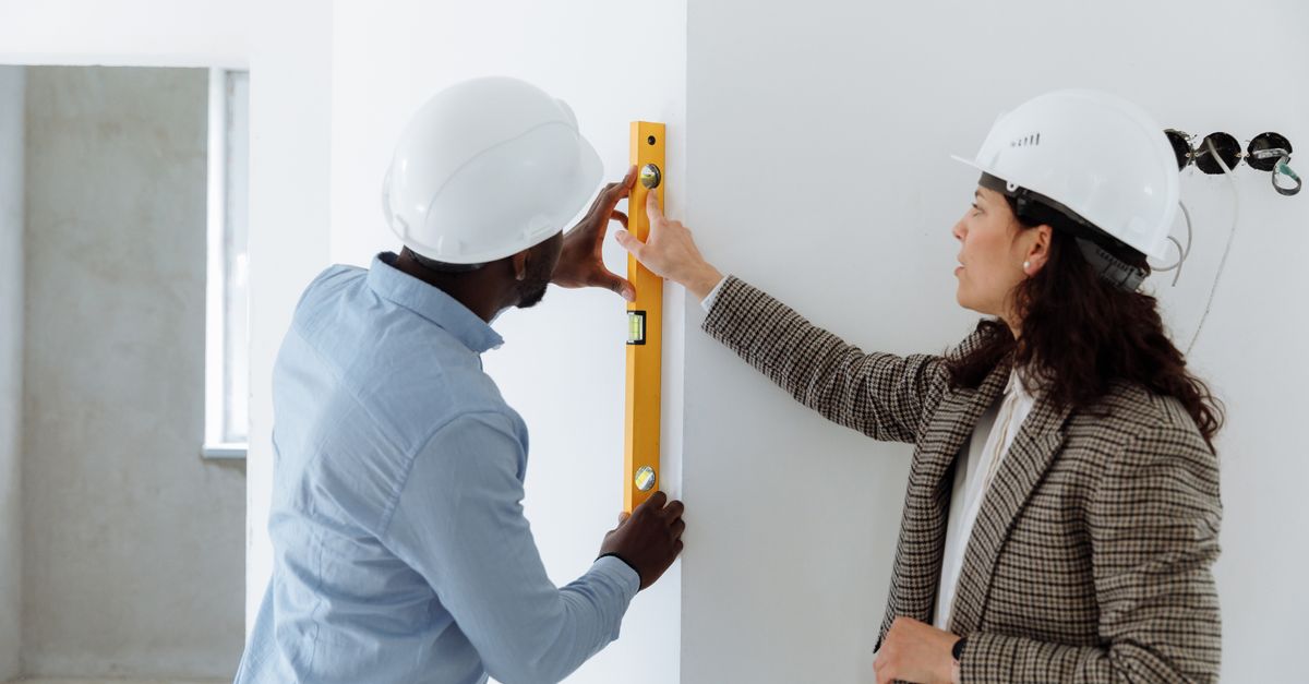 Two contractors using a level bar to check wall alignment inside a building.